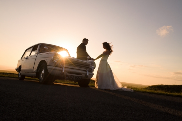 Bride and groom standing by a wedding car as the sun sets - Picture by Tino and Pip Photography